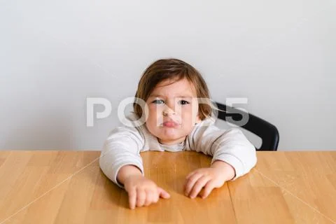 Toddler girl unhappy sitting at wooden desk. Tired child, hungry kid Stock Photos