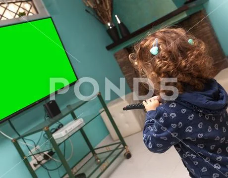Toddler girl watching television with a remote control Stock Photos