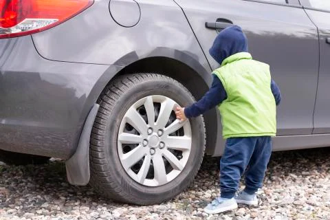 A toddler in a green vest against the background of a gray car Stock Photos