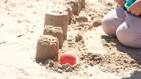 Toddler hand lifting a red plastic mold from a fresh sandcastle row on the be Vidéo 335839406