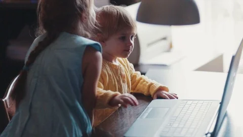 A toddler is having fun with the laptop, elder sister helps with that Stock Footage 69775241