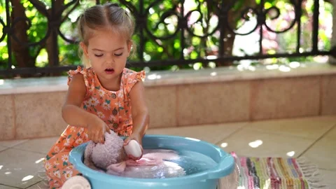 Toddler having fun sharing a bath with stuffed rabbit toy in water bucket Stock Footage 269143376