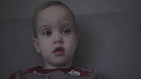 Toddler with high temperature sitting sofa in living room gray pajamas sick baby Stock Footage 242420246