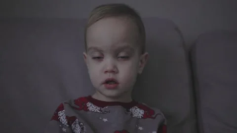 Toddler with high temperature sitting sofa in living room gray pajamas sick baby Stock Footage 242420427