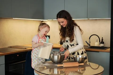 Toddler Holding Flour Container While Mother Sifts in Kitchen Foto stock