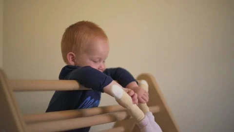 Toddler holding stuffed toy while standing on wooden climbing frame, engaging in Vídeo Stock 295469252