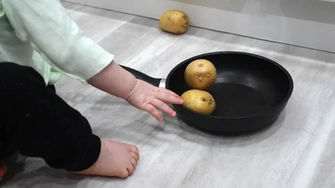 Toddler joyfully plays on the floor with a kitchen skillet and potato Stock Footage 266751012