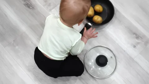 Toddler joyfully plays on the floor with a kitchen skillet and potato Stock Footage 266751111