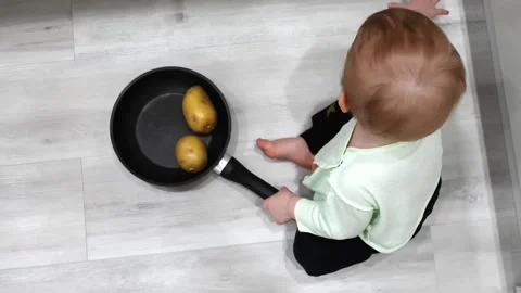Toddler joyfully plays on the floor with a kitchen skillet and potato Stock Footage 266751642