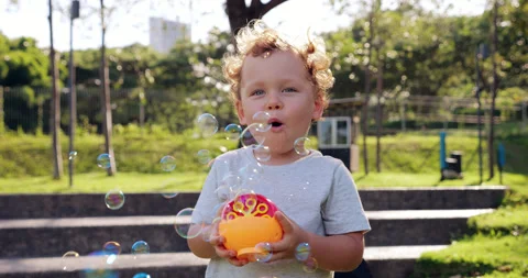 Toddler joyfully plays with small bubble machine, watching soap bubbles fly Stock Footage 277522299