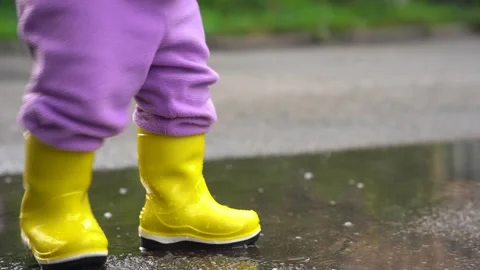 A toddler kid in yellow boots walks through puddles and falls into a puddle Stock Footage 267190836