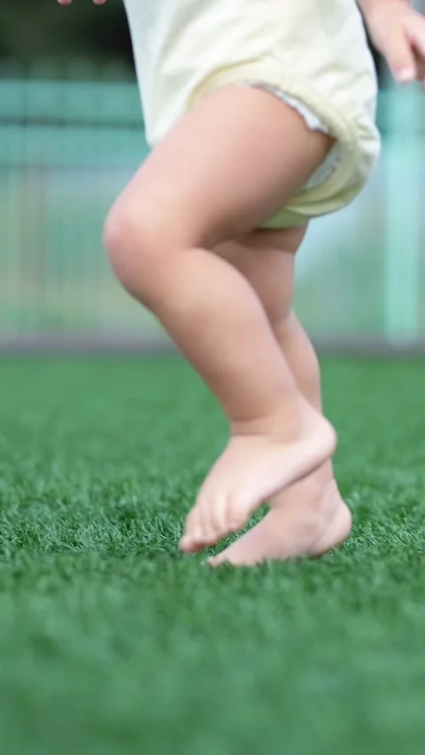 Toddler learning to walk barefoot on green grass taking first steps, a close up Stock Footage 340844323