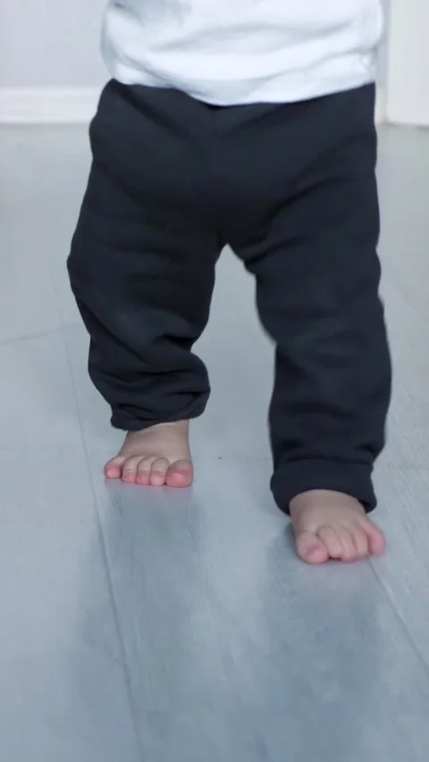Toddler learning to walk barefoot as he takes his first wobbly steps on a wooden Stock Footage 341432875