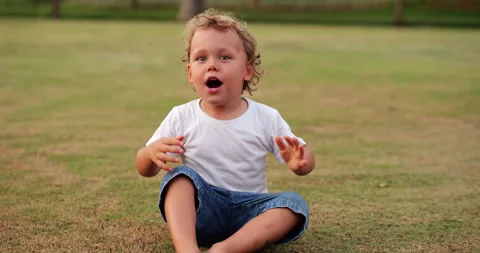 Toddler loudly sings, even shouting, sitting in park, portrait shot. Vídeos de archivo 283902834