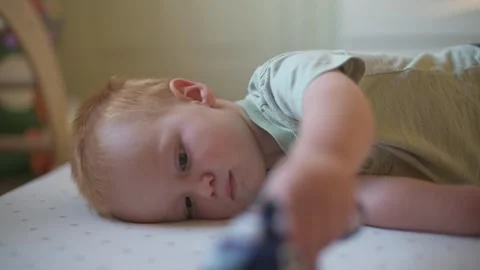Toddler Lying on Mat Playing Thoughtfully with Toy toddler rests on play mat Stock Footage 296089053