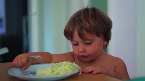 Toddler picking up spaghetti with fingers at the dining table at home, play.. Stock Footage 340430378
