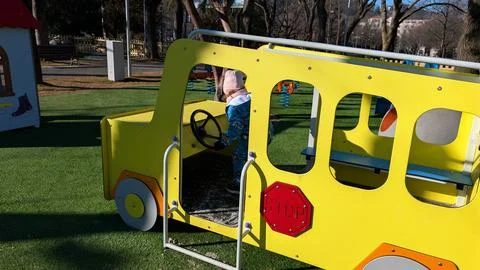 Toddler Playing Driver Inside Bright Yellow Toy Bus on Sunny Playground Foto stock