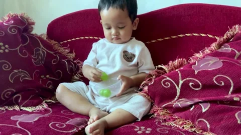 Toddler playing with a grape on a red couch Stock Footage 344104471