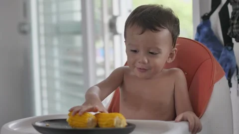 Toddler plays with boiled corn sitting on children high chair Video stock 248281746
