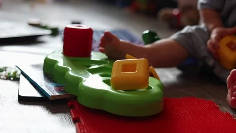 A toddler plays with a colorful plastic shape sorting toy on a textured floor in Stock Footage 345611570