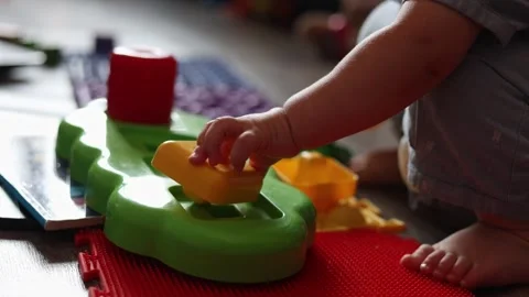 A toddler plays with a colorful plastic shape sorting toy on a textured floor at Stock Footage 345611592