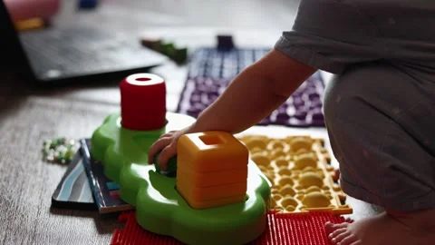 A toddler plays with colorful plastic stacking toys on a textured floor in a Stock Footage 345611585