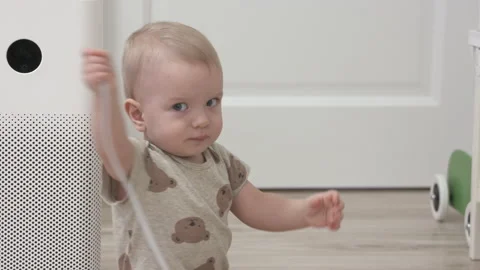 Toddler pulls the electric plug out of socket, 1 year old infant playing with Stock Footage 172368942