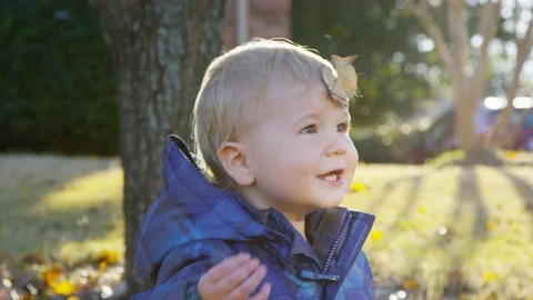Toddler pulls a leaf off of his forehead and laughs as leaves fall around him 스톡 동영상 93890129
