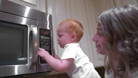 Toddler reaches up to touch microwave controls under watchful eye of a parent Stockbeeldmateriaal 290832146