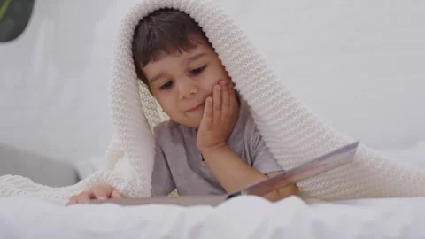 Toddler reading a book on a bed at home Stock Footage 244733499