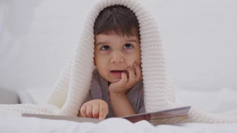 Toddler reading a book on a bed at home and watching on camera Stock Footage 244733557