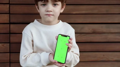 A toddler sits on a bench and looks on the phone with green screen Stock Footage 246769575