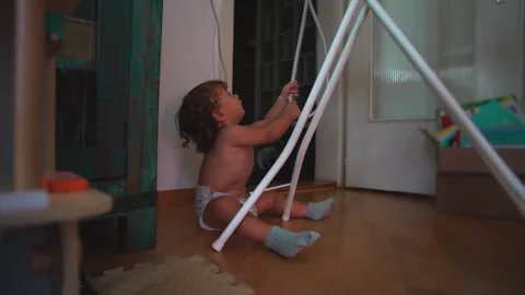 Toddler sitting on floor while pulling hanging rope attached to indoor dryi.. Stock Footage 335680852