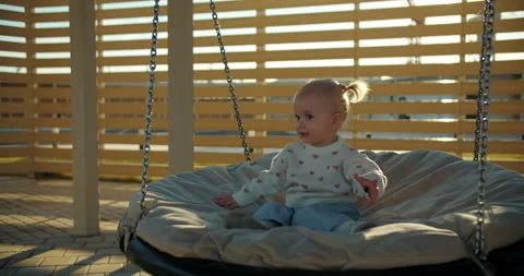 Toddler sitting on round swing under wooden shelter in sunlight Stock Footage 323393324