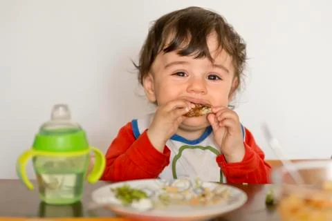 Toddler sitting at table eating Stock Photos