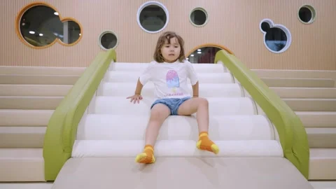Toddler sliding down indoor bumpy playground slide with excitement and fun Stock Footage 289666135