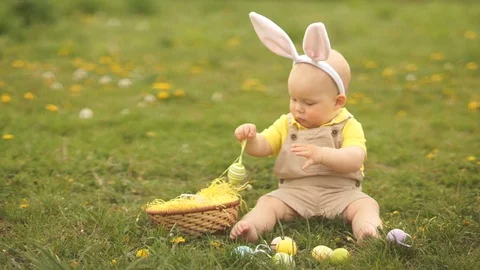 Toddler in a suit of the Easter Bunny plays with Easter eggs sitting on the Stock Footage 115847173
