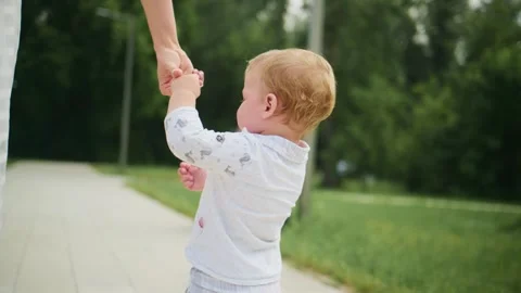 Toddler takes first steps on paved path, guided by parent Stock Footage 340890105