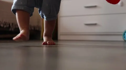 A toddler takes their first steps on a wooden floor in a bright and cozy home Stock Footage 345643240