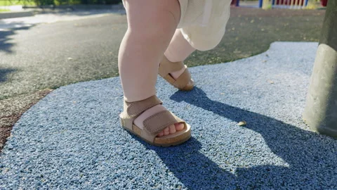 Toddler taking first steps in outdoor playground, wearing beige sandals, on Video stock 314277979