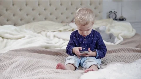 Toddler is using a smartphone on a bad. FULL HD slow motion Stock Footage 73967506