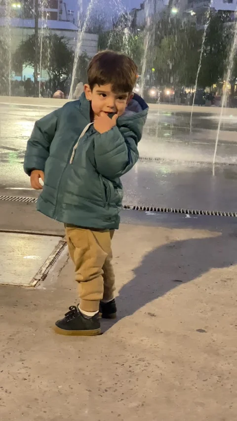 A toddler is walking and jumping in front of a water fountain and laughing in Stock Footage 278333871