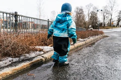 Toddler walking through spring puddle in Nordic city park. Stock Photos