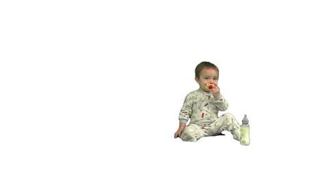 Toddler walks onscreen from left and sits next to his bottle. White background. Stock Footage 49864490