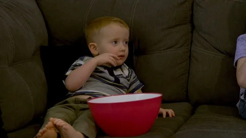 Toddler watching TV and empty popcorn bowl Stock Footage 97147769