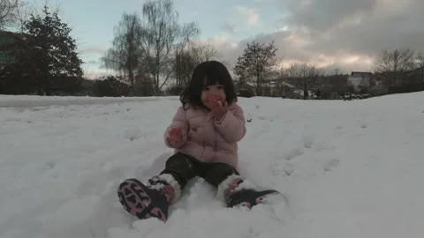Toddler in winter jacket trying to eat fresh snow from the ground. Stock Footage 147210836