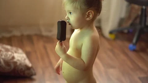 Toddler without clothes eats ice cream in chocolate and watches tv Stock Footage 153132469