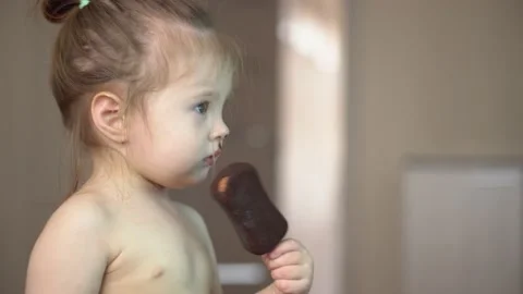 Toddler without clothes eats ice cream in chocolate and watches tv Stock Footage 153132525