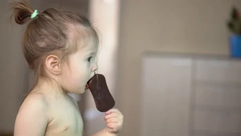 Toddler without clothes eats ice cream in chocolate and watches tv Stock Footage 153132640