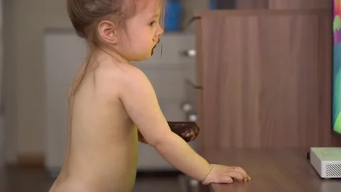 Toddler without clothes eats ice cream in chocolate and watches tv Stock Footage 153132849